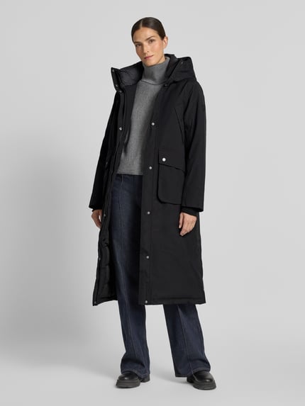 Frauenmodel trägt Regular Fit Parka mit Kapuze Modell 'Melody' von Didriksons, schwarz, aufgesetzte Taschen, elastische Ärmelabschlüsse, Ganzkörperansicht von vorne. Rückenlänge 111 cm, Schulterbreite 42 cm, Brustweite 53 cm, Ärmellänge 65 cm.