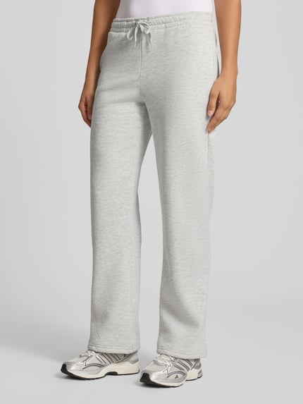 Frauenmodel trägt Wide Fit Sweatpants aus Baumwoll-Mix Modell 'Iconic' von Gina Tricot in Hellgrau, elastischer Bund mit Tunnelzug, Ganzkörperansicht von vorne, Damen Sweatpants, Innenbeinlänge bei Größe S 80 cm.