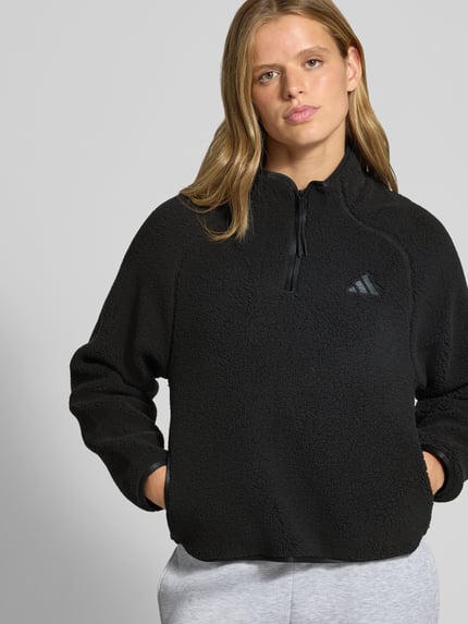 Frauenmodel trägt schwarze Regular Fit Fleecejacke mit Troyerkragen von adidas, flauschige Struktur, adidas Sportswear, Nahaufnahme Oberkörper.
