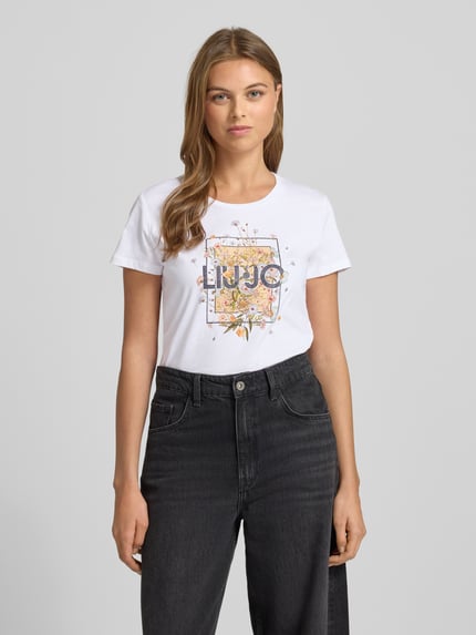 Kobiece modelka nosi Damski t-shirt z nadrukiem z logo i obszyciem ozdobnymi kamieniami, bawełna, krój regular fit, okrągły dekolt, Liu Jo White, długość tyłu 62 cm, rozmiar S, widok całej sylwetki z przodu.