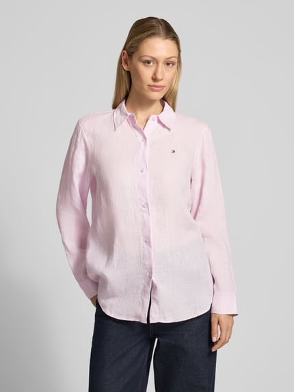 Modelka kobieca ma na sobie Relaxed Fit Langarmbluse aus reinem Leinen od Tommy Hilfiger, jasnoróżowa, gładka, lniana faktura, logo na piersi, krój relaxed fit, kołnierzyk koszulowy, długi rękaw z mankietem, zaokrąglony dół, widok całej sylwetki z przodu.