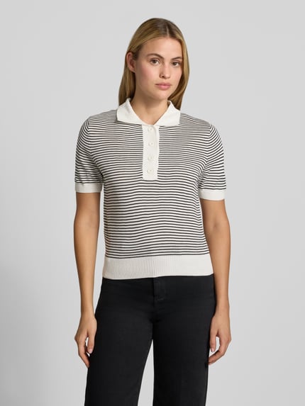Frauenmodel trägt Poloshirt mit gerippten Abschlüssen von MANGO in Weiß-Schwarz mit feinen Streifen, gerade Passform, Polokragen, Halbarm, angenehme Strickstruktur, Ganzkörperansicht von vorne.