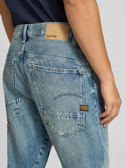 Männermodel trägt blaue, locker geschnittene Jeans aus Baumwolle mit Waschung, sichtbares G-Star RAW Label, Nahaufnahme Rückansicht.