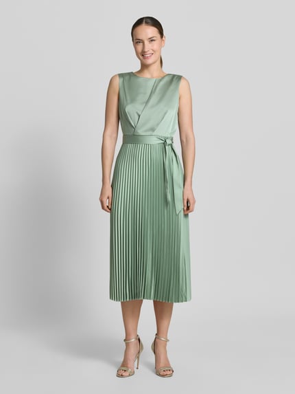 Frauenmodel trägt mintgrünes Midikleid mit Plisseefalten und Bindegürtel von comma aus Material-Mix, A-Linie, Ganzkörperansicht von vorne.