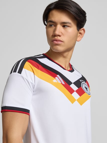 Männermodel trägt DFB Heimtrikot mit Label-Print von adidas Sportswear, Regular-Fit, Rundhalsausschnitt, gerippte Ärmelabschlüsse, Nahaufnahme Oberkörper