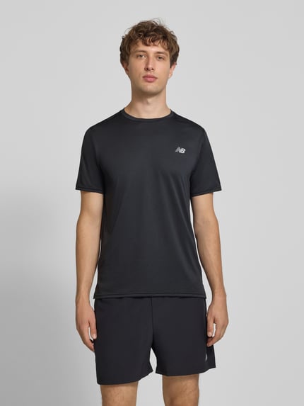Männermodel trägt Funktionsshirt mit Rundhalsausschnitt und Logo von New Balance in Schwarz, glatte Textur, Regular Fit, Ganzkörperansicht von vorne.