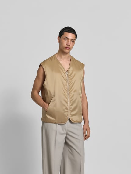Męski model nosi Relaxed Fit Weste in Stepp-Optik od MM6 Maison Margiela, beż, przeszycia, kieszenie, dekolt w serek, zamek, Ganzkörperansicht von vorne.