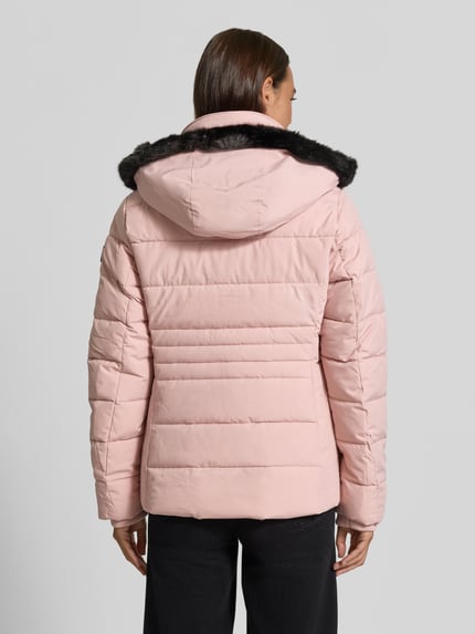 Frauenmodel trägt Jacke mit abnehmbarer Kapuze Modell 'ECLIPSE' von NAUTGÅRD in Rosa, gesteppt, Struktur glatt, Ganzkörperansicht Rückansicht. Gerader Schnitt, gestrickte Ärmelabschlüsse, seitliche Eingrifftaschen mit Druckknopfverschluss, Zweiwege-Reißverschluss, Label-Patch, Kontext gemäß Beschreibung integriert.