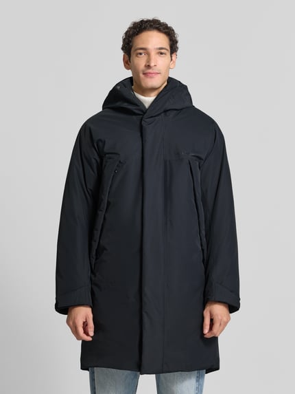 Męski model nosi Regular Fit Parka mit Futter aus Alcantara Modell 'Treeline HIPE' von Peak Performance, kolor czarny, długa, gładka tekstura, podszewka alcantara, zamek błyskawiczny kryty, Długość tyłu w rozmiarze M: 102 cm, Szerokość ramion w rozmiarze M: 52 cm, Szerokość w rozmiarze M: 62 cm, Długość rękawów: 60 cm, zdjęcie całej sylwetki z przodu.
