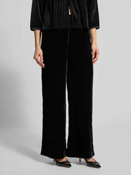 Kobiece modelka nosi spodnie materiałowe z elastycznym pasem OPUS PANTS, model 'Mucia', czarne, luźny krój, wpuszczane kieszenie, widok z przodu, ujęcie całej sylwetki.