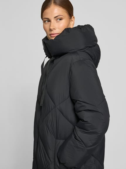 Frauenmodel trägt Puffer Coat mit Zweiwege Reißverschluss von JAKE*S WOMAN CASUAL in Schwarz, Rautensteppung, Oversized, Kapuze, Ganzkörperansicht von vorne.