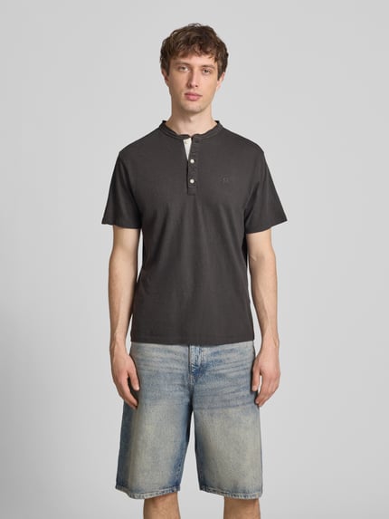 Männermodel trägt T-Shirt mit kurzer Knopfleiste von Superdry in dunklem Ton, Regular-Fit aus Leinen-Baumwoll-Mix mit Polokragen, Logo-Stitching, Rückenlänge bei Größe M 62 cm, Ganzkörperansicht von vorne.