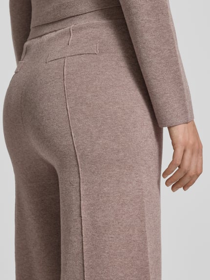 Kobiece model prezentuje spodnie materiałowe z ozdobnymi szwami od Christian Berg Woman, mieszanka wiskozy, elastyczny pas, imitowane kieszenie z tyłu, szeroki krój, zdjęcie z tyłu zbliżenie na dolną część pleców.
