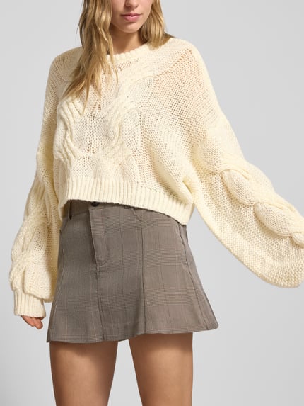 Frauenmodel trägt Cropped Strickpullover mit gerippten Abschlüssen Modell 'LOES' von Noisy May in lockerer Passform, cremefarben, Rundhalsausschnitt, weiche Stricktextur, Nahaufnahme Oberkörper. Rückenlänge bei Größe S 48 cm, Ärmellänge 50 cm.