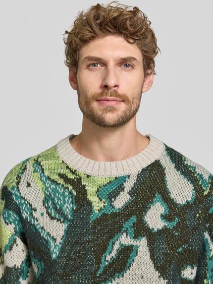 Mężczyzna nosi Regular Fit Strickpullover mit Baumwoll-Anteil von Scotch & Soda, zielone i beżowe kolory, mieszanka materiałów, krój z długim rękawem, okrągły dekolt, prążkowane wykończenia, długość tyłu 67 cm w rozmiarze M, długość rękawów 62 cm w rozmiarze M, zbliżenie na górną część ciała.