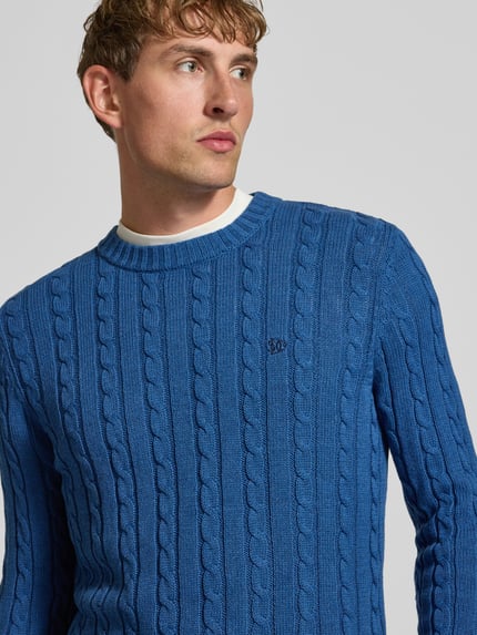 Männermodel trägt Strickpullover mit Zopfmuster und Rundhalsausschnitt von Superdry aus reiner Baumwolle in Blau, Nahaufnahme Oberkörper.
