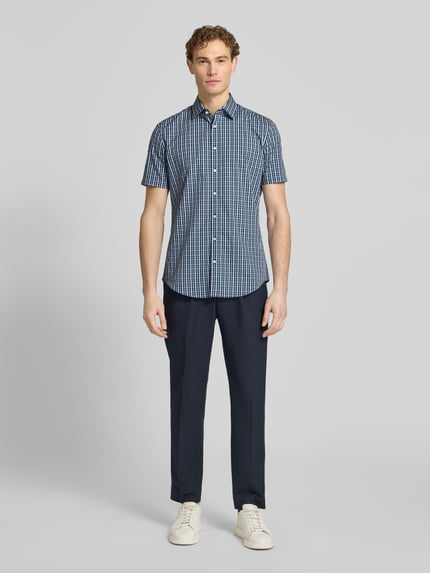 Männermodel trägt Slim Fit Business-Hemd aus Baumwolle mit Kentkragen von Jake*s mit Knopfleiste, 1/2-Arm, kariert, Ganzkörperansicht von vorne. Reine Baumwolle, Rückenlänge 79 cm, Schulterbreite 48 cm, Ärmellänge 23 cm.