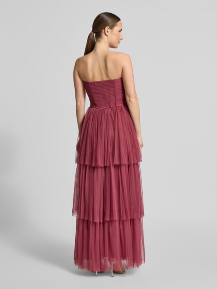 Frauenmodel trägt Regular Fit Abendkleid mit Rüschenbesatz von LACE & BEADS aus bordeauxfarbenem Mesh, tailliert, schulterfrei, A-Linie, Ganzkörperansicht Rückansicht.