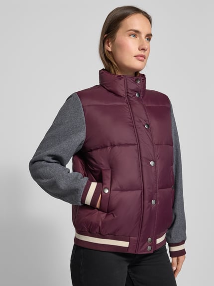 Frauenmodel trägt Steppjacke mit Stehkragen von Milano Italy in Dunkelrot mit grauen Ärmeln, Rippsäumen und Eingrifftaschen, Nahaufnahme Oberkörper. Rückenlänge 62 cm, Schulterbreite 42 cm, Brustweite 54 cm, Ärmellänge 63 cm, Regular Fit, verdeckter Reißverschluss, Druckknopfleiste.