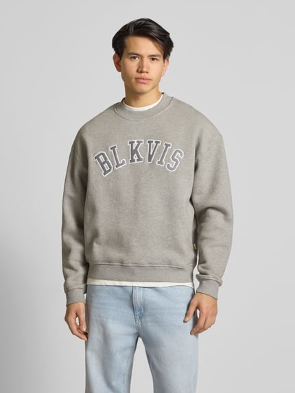 Männermodel trägt Sweatshirt mit Logo und Rundhalsausschnitt von BLKVIS in Grau, reine Baumwolle, Relaxed Fit, Ganzkörperansicht von vorne.
