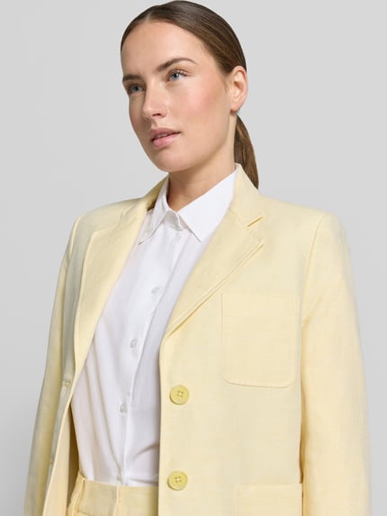 Frauenmodel trägt Blazer aus Leinen-Mix mit Reverskragen und Brusttasche von MICHAEL Michael Kors, hellgelb, Nahaufnahme Oberkörper. Gerader-Schnitt, Knopfverschluss, Aufgesetzte Eingrifftaschen, Rückenlänge 64 cm, Brustweite 48 cm, Ärmellänge 62 cm.