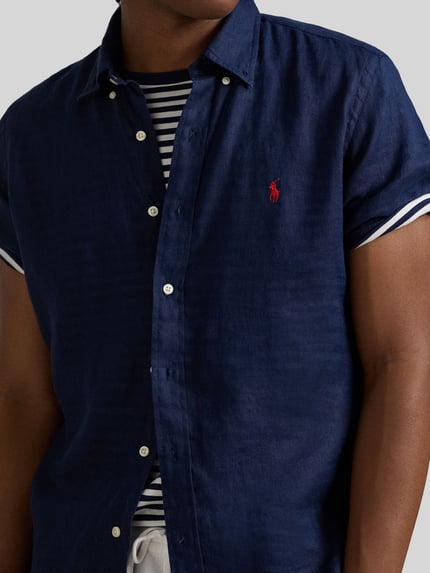 Mannenmodel draagt Regular Fit Leinenhemd met Button-Down-Kragen van Polo Ralph Lauren, look: effen kleuren, regular fit, button-downkraag, doorlopende knoopsluiting, gestikt logo, korte mouw, licht afgeronde rompzoom, materiaal: puur linnen, detailopname bovenlichaam.