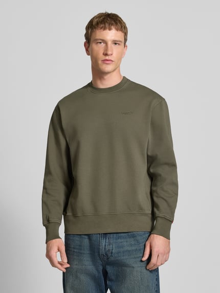 Męski model nosi Sweatshirt mit Rundhalsausschnitt und Label-Stitching od Levi's®, czysta bawełna, krój regular fit, kolor khaki, ujęcie całej sylwetki z przodu.