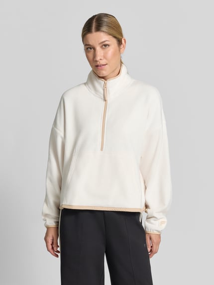Frauenmodel trägt Relaxed Fit Pullover Troyer-Kragen Modell 'Polar' von Fabletics, Damen Fleecejacke in Creme mit Kängurutasche und überschnittenen Schultern, weich strukturierte Fleece-Textur, Ganzkörperansicht von vorne.