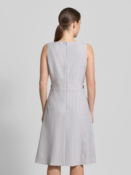 Kobieta modelka nosi Knielanges Kleid aus Seersucker mit Streifen und Lurex von Christian Berg Woman Selection, szare paski z lurex, linia a, okrągły dekolt, długość do kolan, faktura tkaniny seersucker, długość tyłu w rozmiarze 36: 100 cm, szerokość w rozmiarze 36: 45 cm, widok całej sylwetki z tyłu.