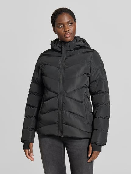 Frauenmodel trägt Regular Fit kurtka z efektem pikowania Model 'Synria' od Cars Jeans, kaptur ze stójką, wpuszczane kieszenie, zamek błyskawiczny, długość tyłu w rozmiarze S: 65 cm, szerokość ramion w rozmiarze S: 42 cm, szerokość w rozmiarze S: 50 cm, długość rękawów w rozmiarze S: 70 cm, czarny kolor, gładka tekstura, Ganzkörperansicht von vorne.