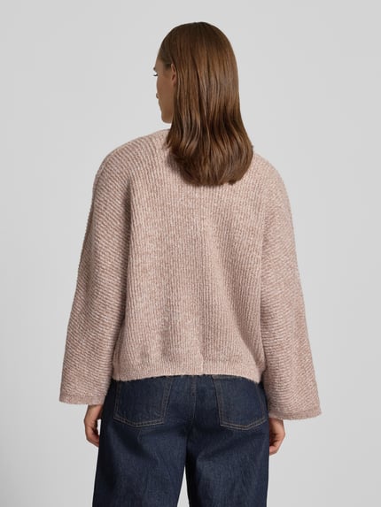 Modelka nosi różową damską Strickjacke mit V-Ausschnitt Modell 'RENE' od Topshop o fakturowanym splocie, relaxed fit, długość tyłu 60 cm, długość rękawa 78 cm, struktura swetra i dżinsy, widok całych pleców