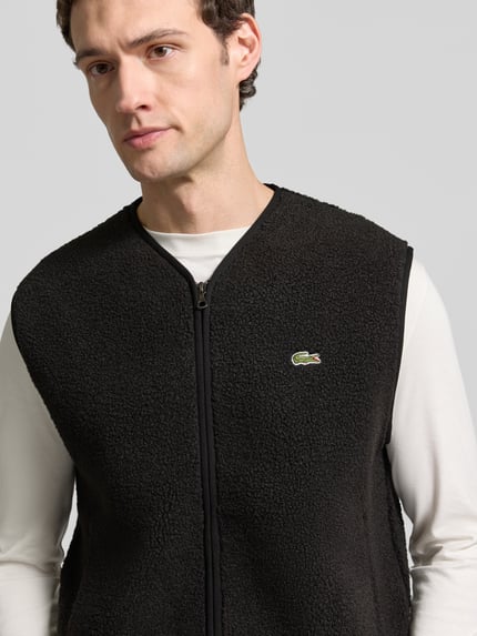 Männermodel trägt Weste mit Fleece-Struktur von Lacoste, unifarben, mit Logo-Patch und Reißverschlusstaschen, Nahaufnahme Oberkörper.