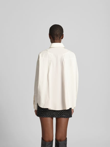 Frauenmodel trägt Regular Fit Hemdbluse aus Baumwolle von MM6 Maison Margiela in Creme mit Hemdblusenkragen, Ganzkörperansicht Rückansicht.