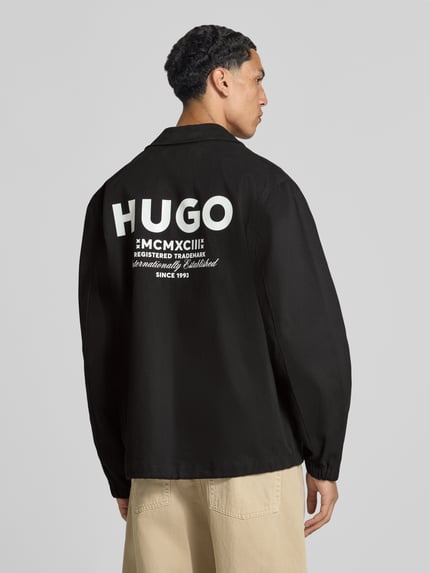 Männermodel trägt schwarze Regular Fit Bomberjacke / Blouson aus reiner Baumwolle Modell 'Biyo2631' von HUGO, Herren Bomberjacke, Ganzkörperansicht Rückansicht.