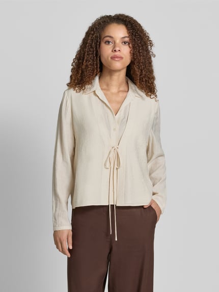 Kobiece modelka nosi bluzka 'Bluse aus Viskose-Mix mit Binde-Detail' von Jake*s Collection, mieszanka wiskozy, krój straight fit, wykładany kołnierz, listwa guzikowa, wiązany detal, długość tyłu w rozmiarze 38: 55 cm, długość rękawów w rozmiarze 38: 62 cm, kolor jasny beż, tekstura lekko prążkowana, widok całej sylwetki z przodu.