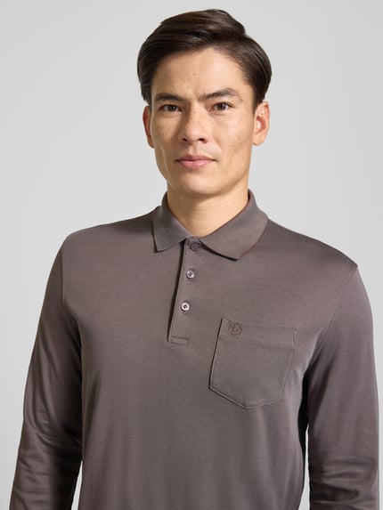 Männermodel trägt Regular Fit Poloshirt aus Mieszanka bawełny mit brustasza von bugatti, Wyhaftowane logo, kołnierzyk polo, krój z długim rękawem, zakończenia rękawów elastyczne, długość tyłu w rozmiarze M: 71 cm, kolor brązowy, gładka faktura, Nahaufnahme Oberkörper.