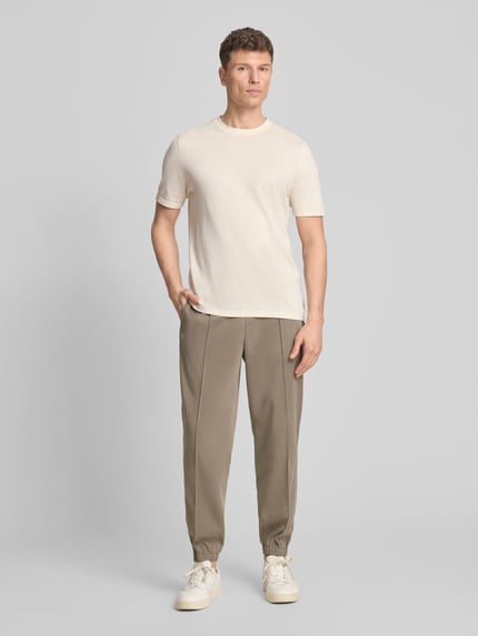 Męski model nosi Regular Fit Stoffhose aus Viskose-Mix mit elastischem Bund od ARMANI EXCHANGE, kolor beżowy, ozdobne szwy, elastyczne zakończenia nogawek, kieszenie z tyłu, szerokość w rozmiarze 32: 44 cm, długość wewnętrzna nogawki: 77 cm, ganzkörperansicht von vorne.