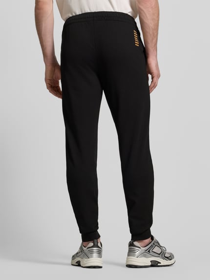 Männermodel trägt Sweatpants mit Logo und elastischem Bund von EA7 Emporio Armani, Schwarz, Regular Fit, Ganzkörperansicht Rückansicht.