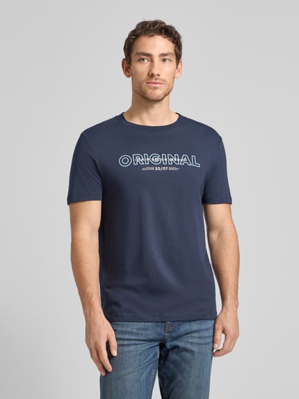 Męski model nosi Regular Fit T-Shirt aus reiner Baumwolle od Tom Tailor Denim, efekt: jednolity kolor, krój regular fit, z napisem z logo, okrągły dekolt, krótki rękaw, bawełna; zdjęcie całej sylwetki z przodu.
