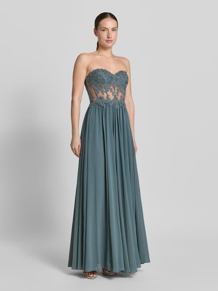 Frauenmodel trägt Abendkleid mit Spitze und Gehschlitz von Mascara in Blau, Maxikleid mit Herz-Ausschnitt und Strasssteinbesatz, semitransparent, Ganzkörperansicht von vorne.
