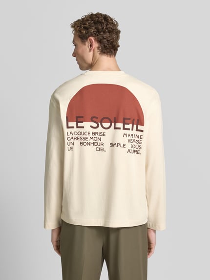 Männermodel trägt Relaxed Fit T-Shirt aus reiner Baumwolle Modell 'AXMAX' von Selected Homme in Creme mit braunem Print, Herren T-Shirt, Ganzkörperansicht Rückansicht.