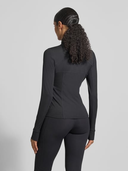 Modelka kobieca ma na sobie Slim Fit Jacke mit Stehkragen Modell 'Storm' od Fabletics, czarna, elastyczna tkanina, krój slim fit, detaliczne szwy, tylna długość 61 cm, szerokość w rozmiarze S: 43 cm, długość rękawa 66 cm, widok całej sylwetki z tyłu.