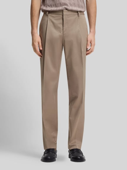 Męski model nosi spodnie z zakładkami w pasie Slim Fit Bundfaltenhose aus Baumwoll-Mix Modell 'GENRICH' od HUGO, efekt: jednolity kolor, mieszanka bawełny, aplikacja z metką, zakładki w pasie, kanty, szlufki na pasek, wpuszczane kieszenie z przodu, kieszenie z tyłu na guzik, zapięcie na haftkę i ukryty zamek błyskawiczny, Ganzkörperansicht von vorne.
