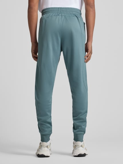 Männermodel trägt Sweatpants mit elastischem Bund von Under Armour in Blaugrün, lockerer Schnitt, Eingrifftaschen, Ganzkörperansicht Rückansicht.