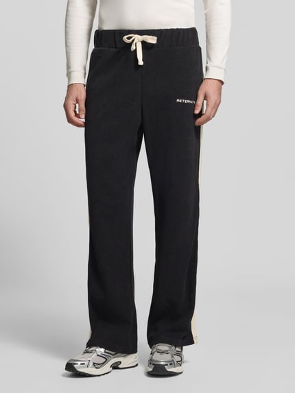 Männermodel trägt Straight Fit Sweatpants aus elastischem Material-Mix von RETERNITY, schwarze Farbe, Label-Stitching, Ganzkörperansicht von vorne.
