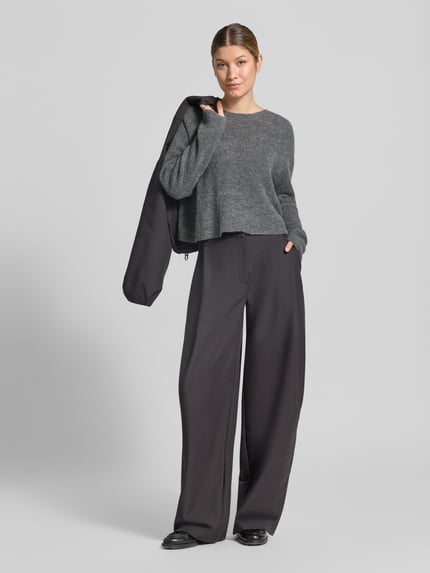 Vrouwenmodel draagt gebreide pullover uit alpacamix met wol van DRYKORN, Model 'MENY', los model, grijs, doorgaande structuur, Ganzkörperansicht von vorne.