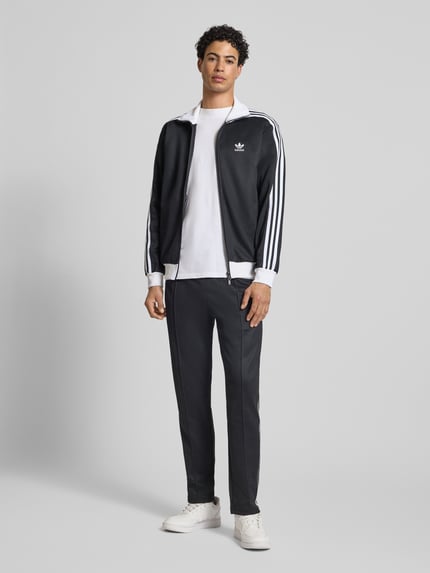 Mannenmodel draagt Sweatjacke mit Reißverschluss van adidas Originals in zwart-wit, katoenmix, losse pasvorm, geribde boorden, recht van voren, geheel lichaamsbeeld.