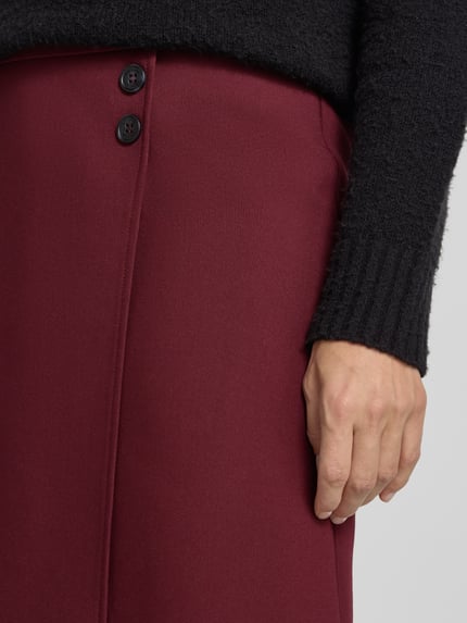 Frauenmodel trägt Minirock mit Viskose-Anteil von MORE & MORE, weinrote Farbe, glatte Textur, Nahaufnahme Oberkörper.