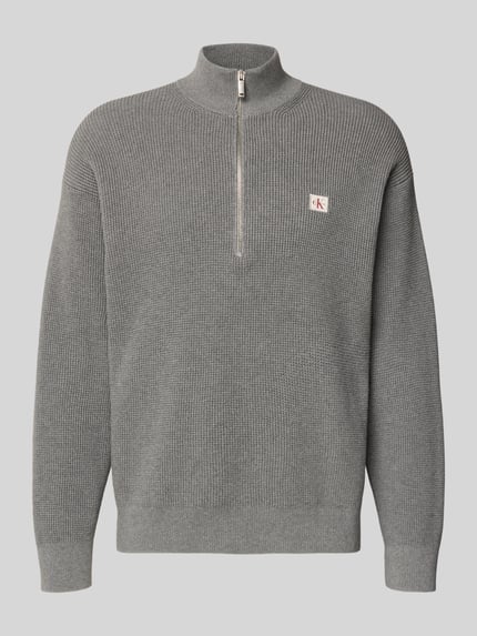 Produktfoto, Loose Fit Troyer mit gerippten Abschlüssen von Calvin Klein Jeans aus grauem Strick, Troyer-Kragen, kurzem Reißverschluss, Label-Detail.