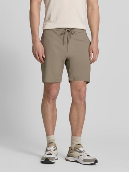 Männermodel trägt Straight Fit Shorts mit Eingrifftaschen Modell 'Drift' von SCANDINAVIAN EDITION, beige, elastischer Bund, Ganzkörperansicht von vorne.